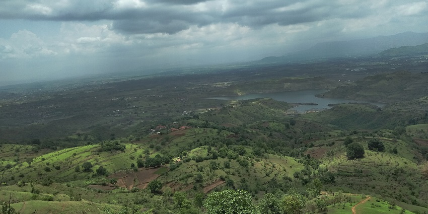 Aerial view of Bhivpuri green hills and a lake under dramatic monsoon clouds.