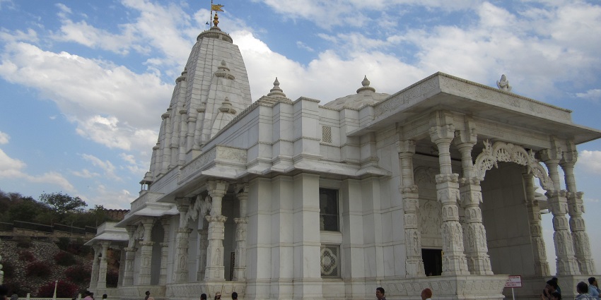 A white marble Birla Mandir featuring ornate carvings against a partly sunny, partly cloudy sky.