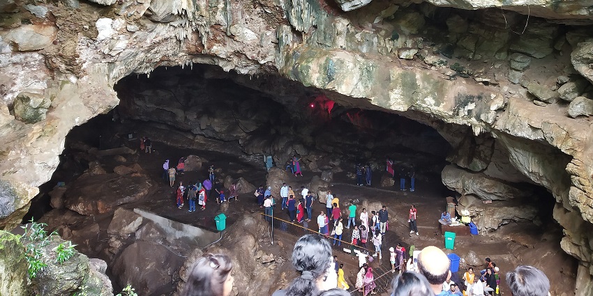 Visitors explore the large rocky cave interior with jagged ceiling and dimly lit passages.