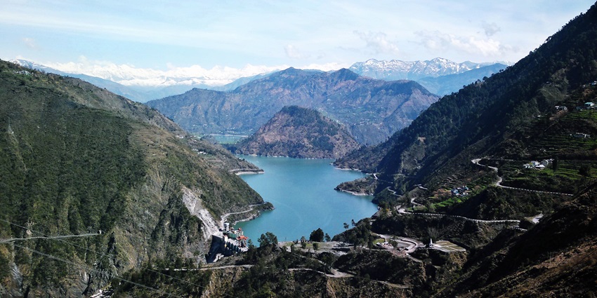 Chamera Lake from above in Himachal Pradesh with distant curvy roads, buildings and mountains.