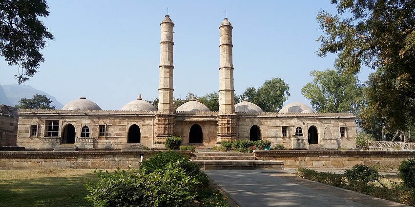 Historic stone mosque with twin minarets, and arched windows surrounded by greens.