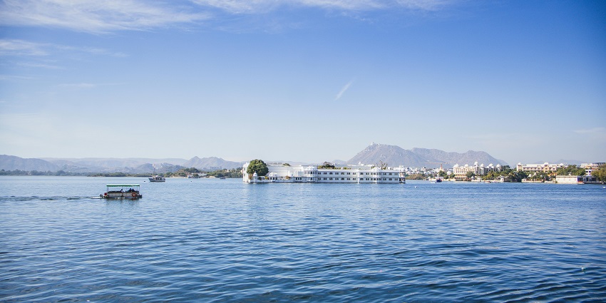 A lone boat floating on the calm waters of Chandlai Lake with hills in the distance.