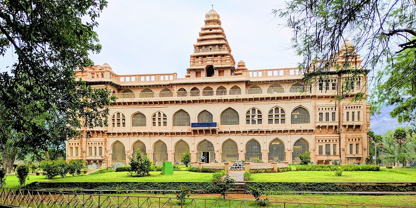 Grand heritage building with arched windows and a well-maintained garden in front.