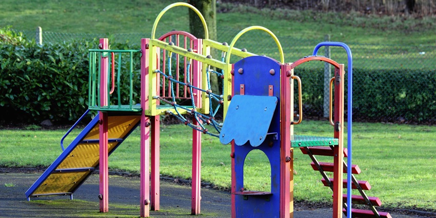 Children’s slide in Chetak Park with vibrant colourful build, green grass and fencing in the back.