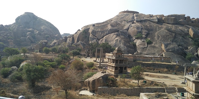 Chitradurga Fort with stone structures, rocky hills, and sparse trees under a clear sky.