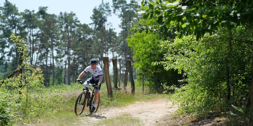 Man riding a bicycle while wearing the riding equipment and surrounded by greenery
