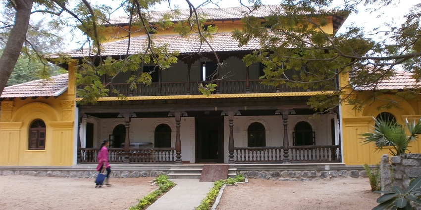 A traditional yellow Karnataka house sits on DakshinaChitra, Chennai, while a visitor walks by