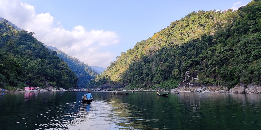 Umngot River with a person on a boat, rocky shores and green mountains places to visit near Barapani.
