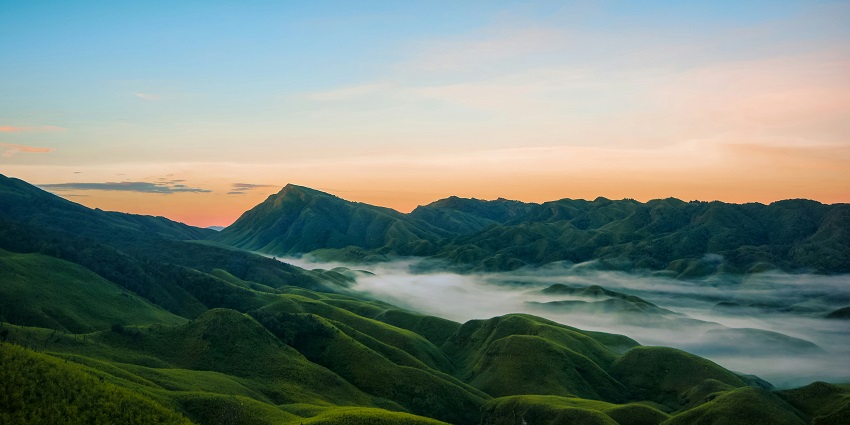 Green hills of Dzüko Valley during sunrise with scattered white clouds.