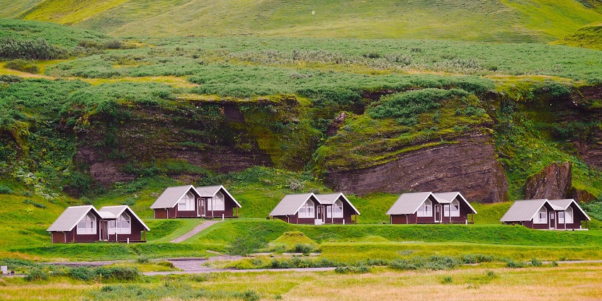 A grassy valley with scattered wooden houses and hills, one of the most peaceful places to visit near Kohima.