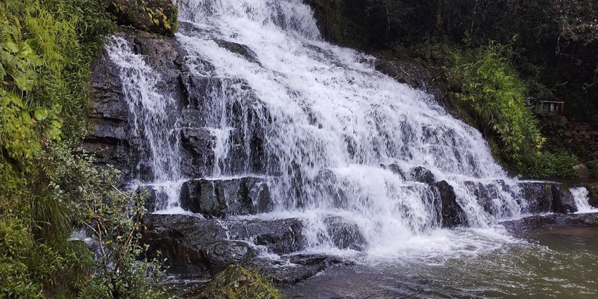 Elephant falls in Shillong with water flowing on the rocky surface and surrounded by greenery.
