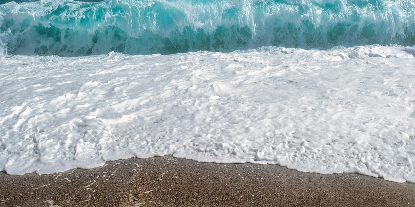Sandy shore of Elliot's Beach with waves crashing gently under a clear sky.