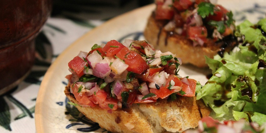 Bruschetta is served on a plate with fresh tomatoes, basil, and toasted bread slices.
