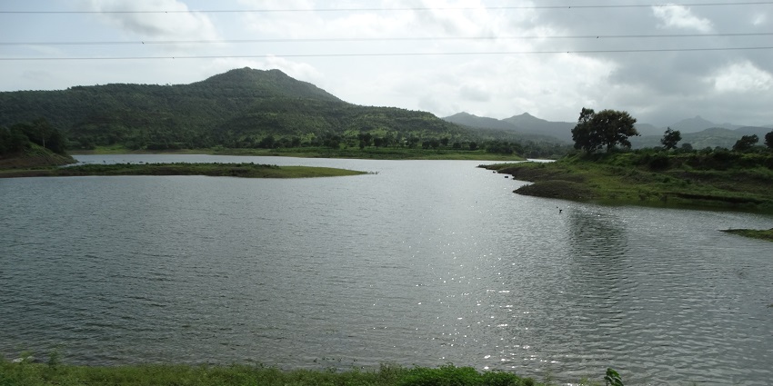 A view of Gadeshwar Dam includes greenery, hills in the background, and serene water.