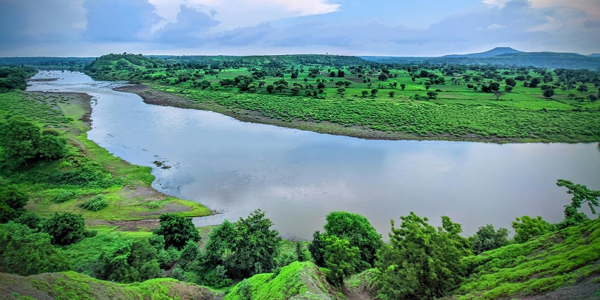 Peaceful riverside view at Gadiara with trees and calm waters at confluence point.