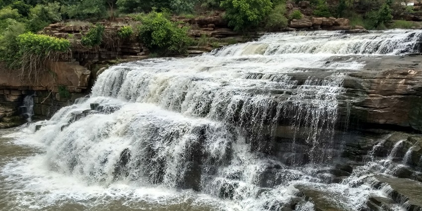 Scenic view of Godachinmalki Falls in Karnataka, India, cascading over rocky green terrain.
