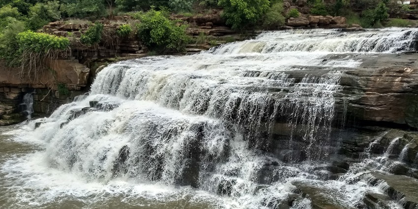 Godchinamalaki falls with water flowing at high pressure on the rocky surface and greenery.