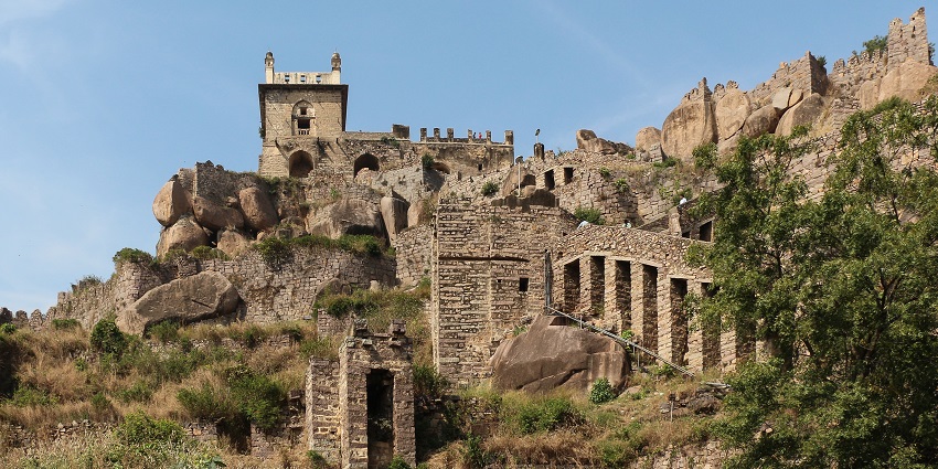 Ancient stone walls and remains of Golconda Fort against a clear, green-blue sky, one of the best places to visit near Gachibowli.