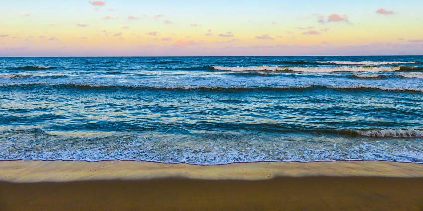 Golden sunset over a calm beach with gentle waves lapping against the sandy shoreline.