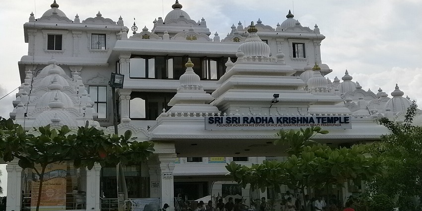 White-marble ISKCON Temple Chennai with ornate towers and lush plants at the entrance