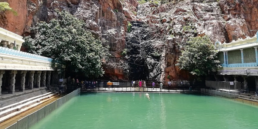 Crowds line up around a green water container between rocky hilltops and temple buildings, one of the best places to visit near Tirupati in one day.