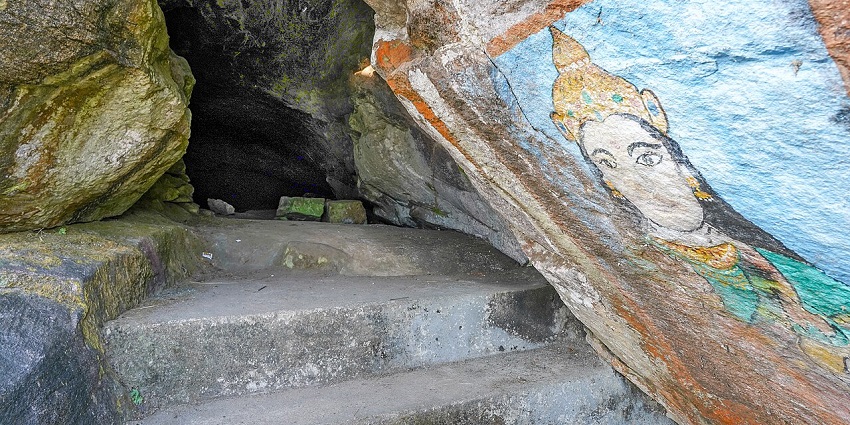 Stone steps leading into a cave entrance with a colourful deity painting on the rock wall