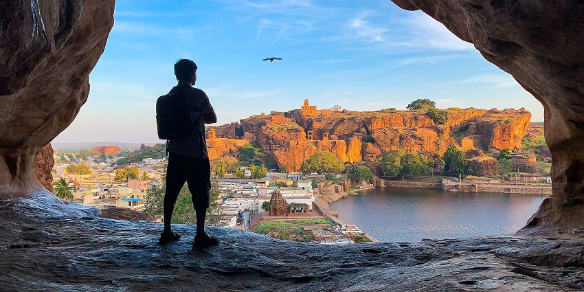 A man standing near the edge of an opening in a cave enjoys the view of a lake, one of the best places to visit near Dandeli.