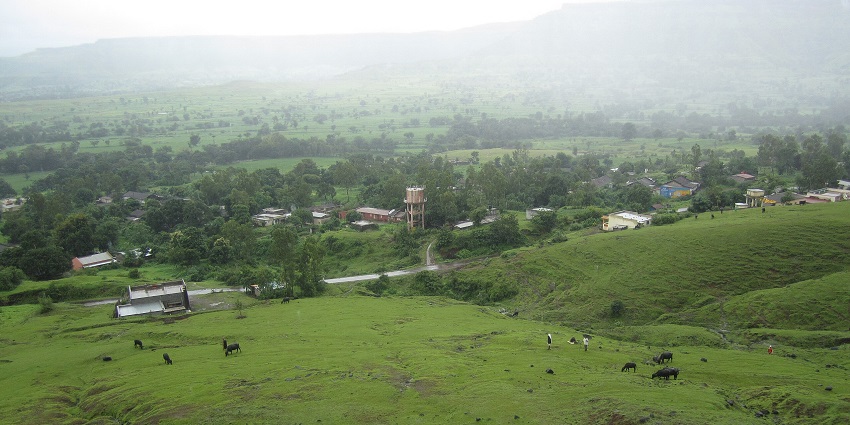 Lush green hilly landscape with grazing cattle, scattered homes, and misty mountains.
