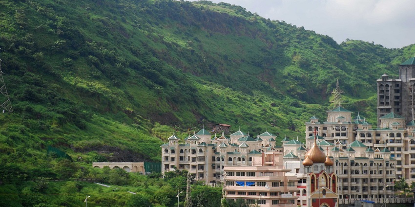 Ornate buildings with towers set against green hills and a partly cloudy, bright sky.