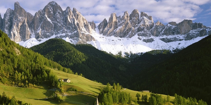 Lush green mountains in Khirsu with snow-capped peaks visible in the distant background.
