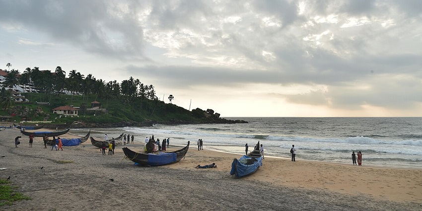 Scenic Kovalam Beach with fishing boats, golden sand, and cloudy evening sky