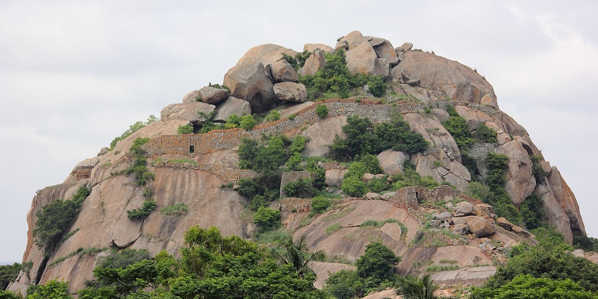 A boulder-strewn hill with greenery and an old fort, one of the places to visit near Kaiwara.
