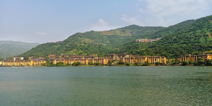 Tranquil Lavasa lake with reflections of distant colorful buildings and hills.