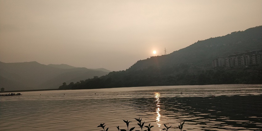 Sunset over a lake with mountain silhouettes, and rippling water in the foreground, one of the best places to visit near Pune in monsoon for couples.