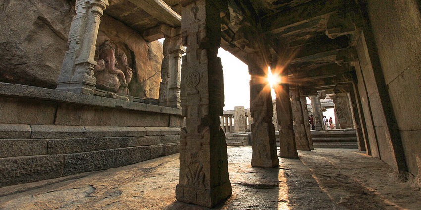 Sunlit stone-pillared corridor at Lepakshi Temple, with a visible Ganesha idol at the end.