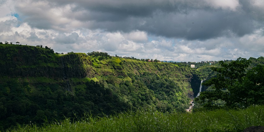 Lush green valley with scattered trees and misty hills under cloudy sky, one of the places to visit near Mumbai for 2 days.