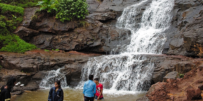 A small waterfall cascading over rocks, with people standing in the water at the base, one of the best places to visit near Pune in monsoon for couples.