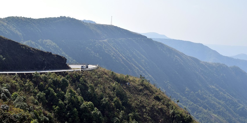 Lum Sohpetbneng Peak with a distant curvy road and dense green mountain landscape.
