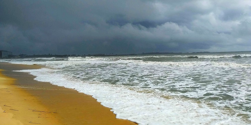 The Malpe beach, where the sea is crashing in waves on the shore under a cloudy sky.
