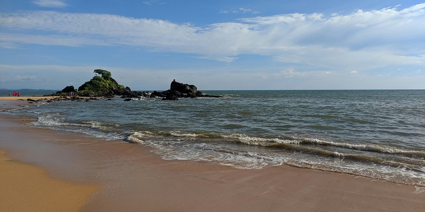 Waves gently lapping the sandy shore at Maravanthe Beach with clear skies and calm waters.
