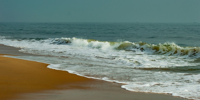 Marina beach with incoming high tide waves, people on the sandy shoreline, and a cloudy sky.
