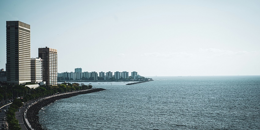 A scenic view of Marine Drive with the coastline and city skyline in the distance.
