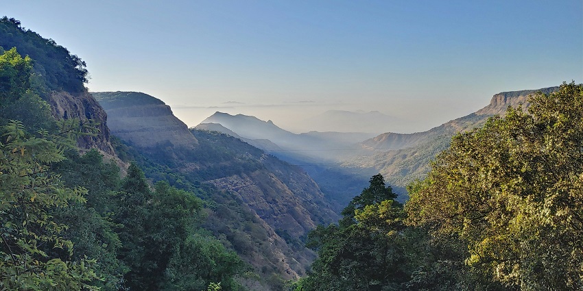 Scenic rocky hills and dense green forests in Matheran under a clear blue sky.