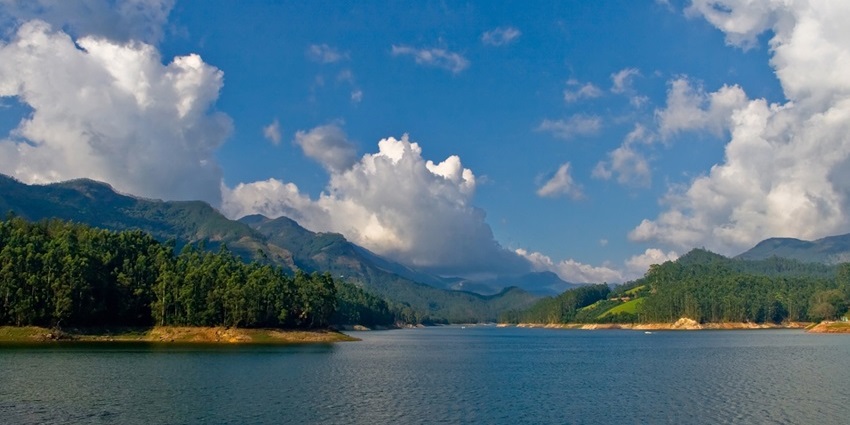 A large water body of the Mattupetty dam reservoir with calm water, distant greenery, and mountains.