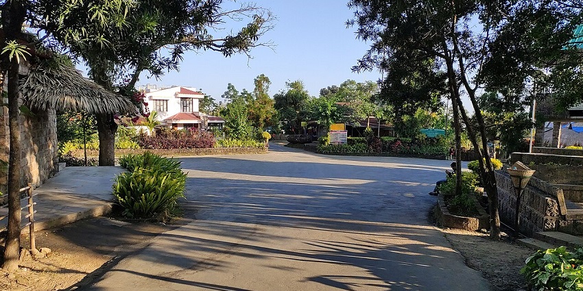 Mawlynnong village in Meghalaya with distant buildings & houses, an empty street and greenery.
