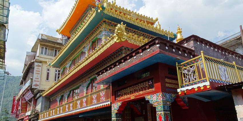 Main street in McLeod Ganj with a traditional Buddhist temple, detailed architecture and people walking.