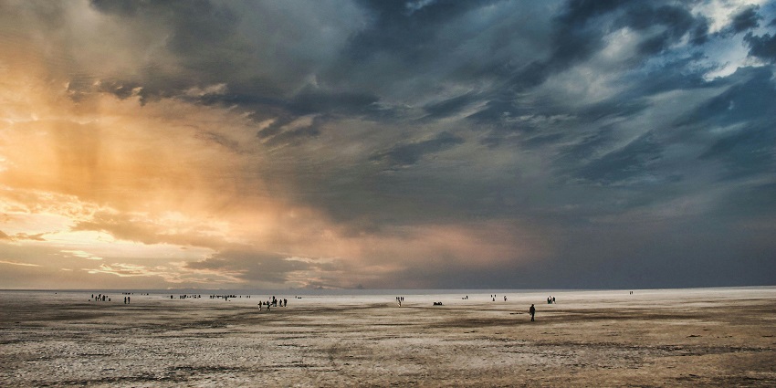 Monsoon sunset over Rann of Kutch with cloudy skies and shimmering wet salt plains.
