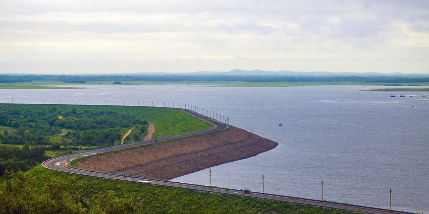 Mukutmanipur dam with a large water body, poles near the water, greenery, and distant mountains.