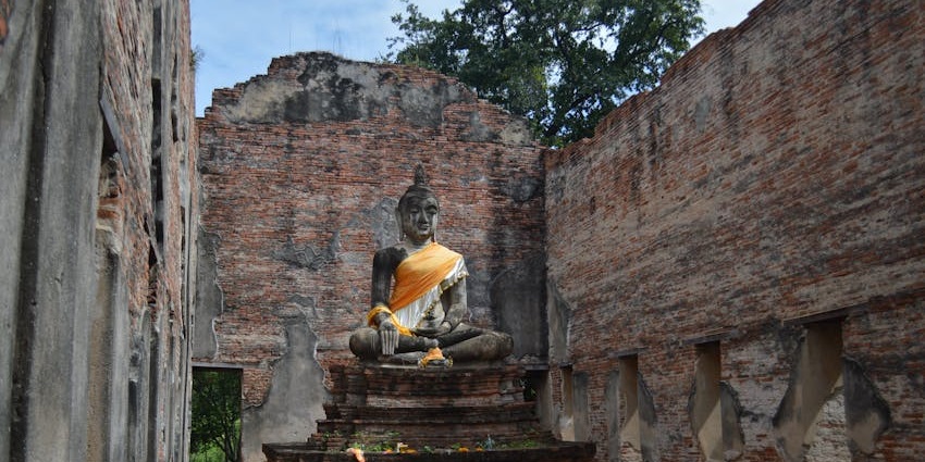 Ancient Buddha statue inside ruined brick temple, weathered stone and soft light