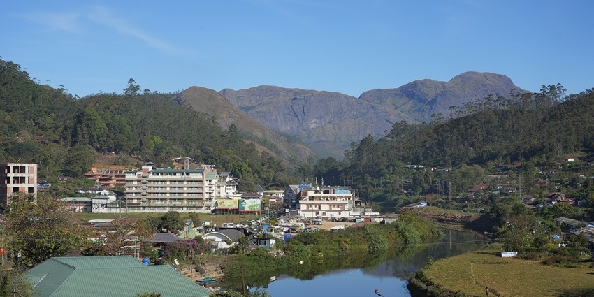 Munnar town in Kerala with calm water, green trees, buildings, and mountains.